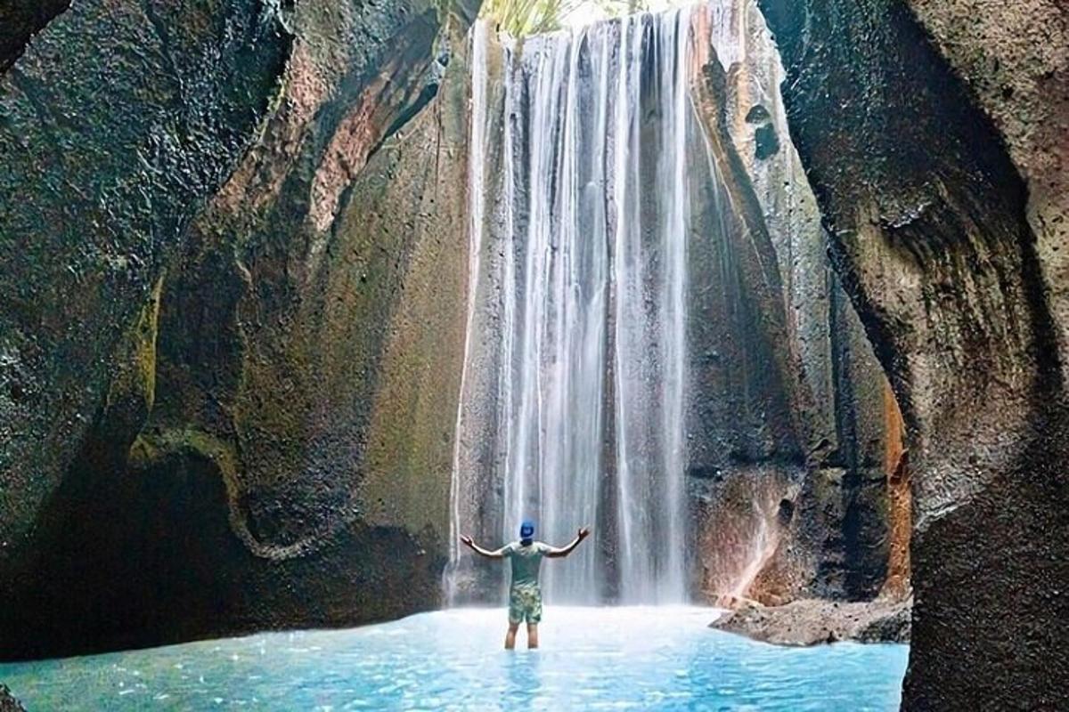 seorang lelaki berdiri di dalam air di hadapan air terjun