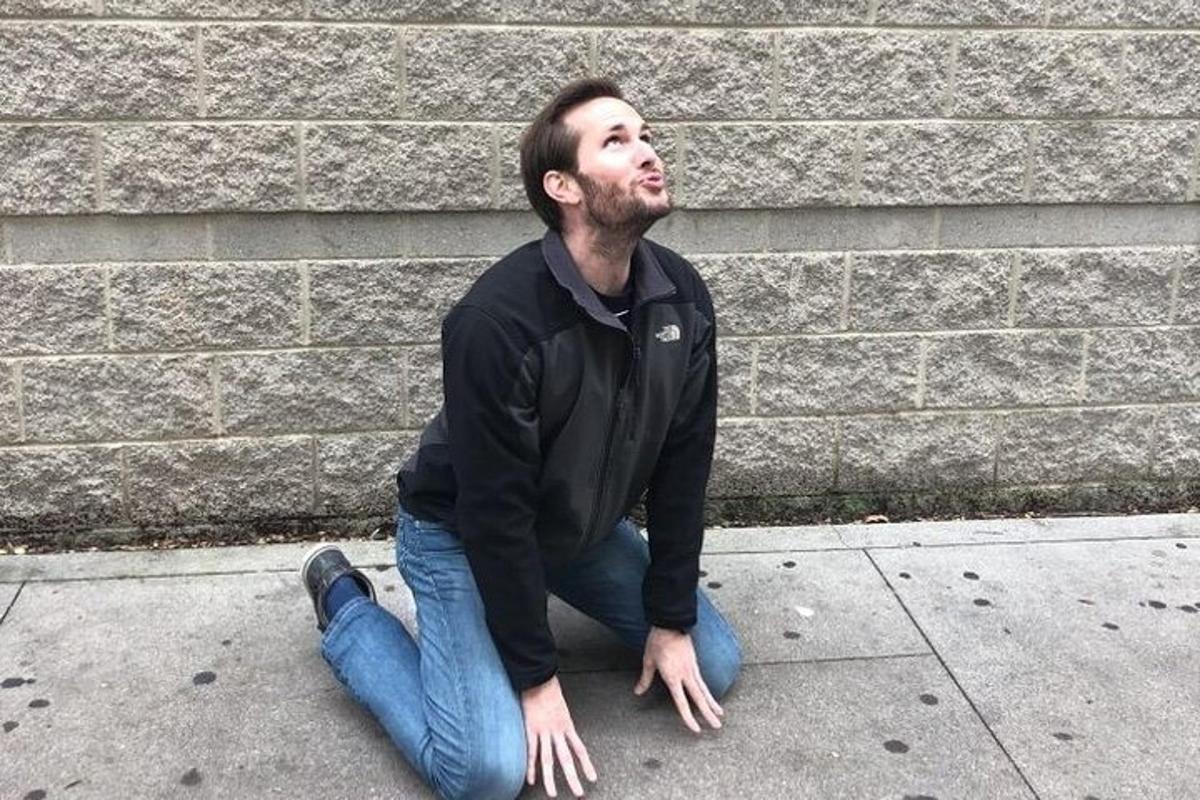 Ein Mann sitzt auf dem Bürgersteig vor einer Backsteinmauer