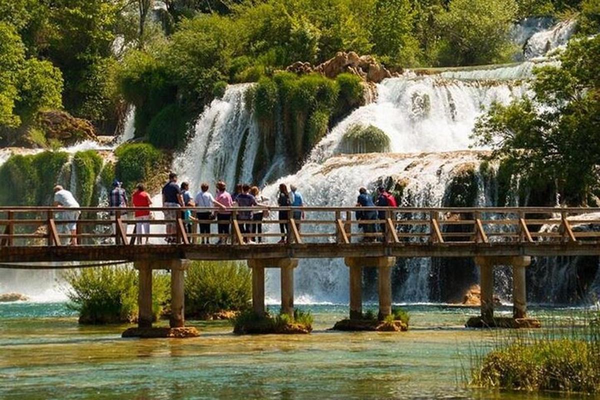 a group of people standing on a bridge in front of a waterfall
