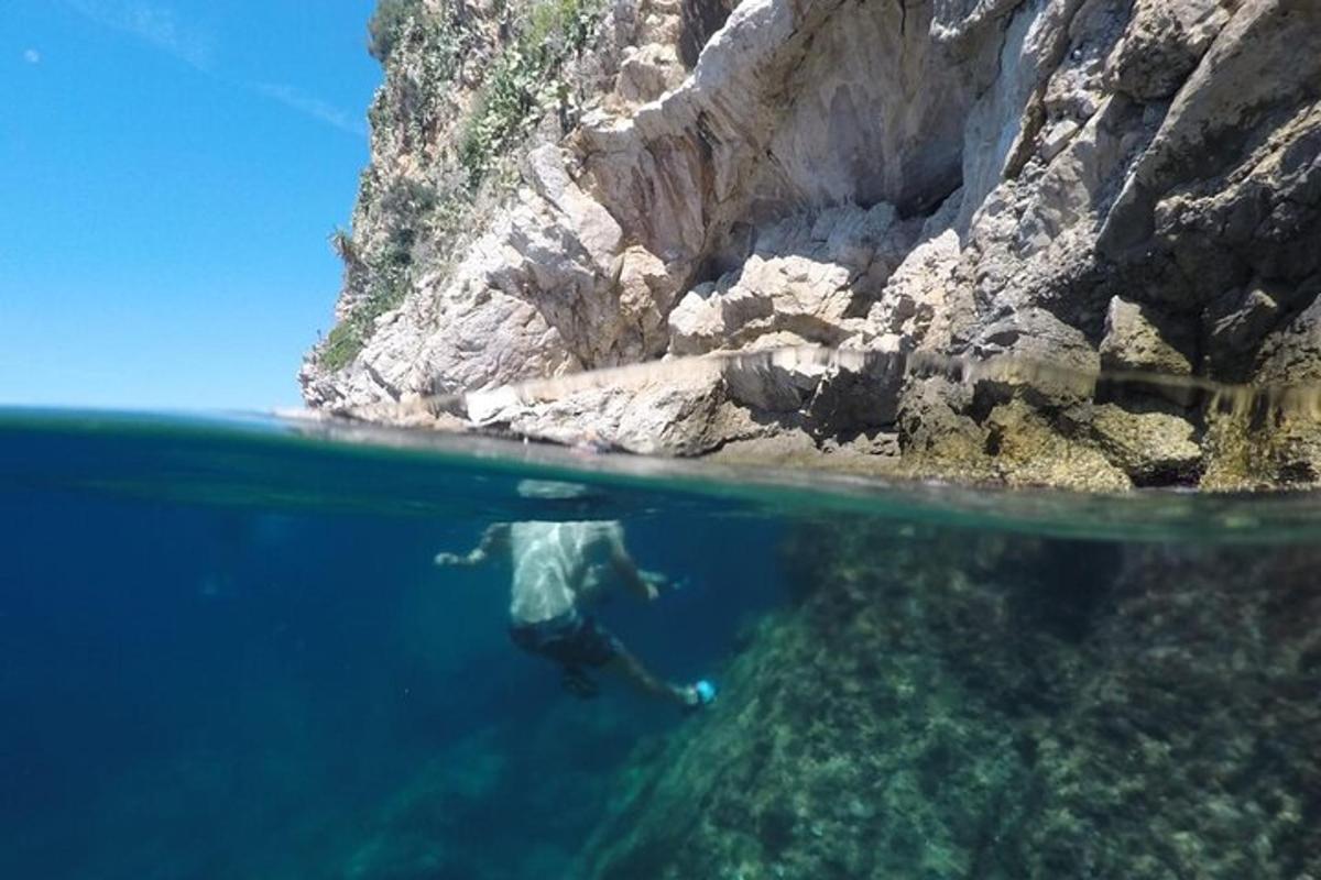 muž plave ve vodě vedle útesu