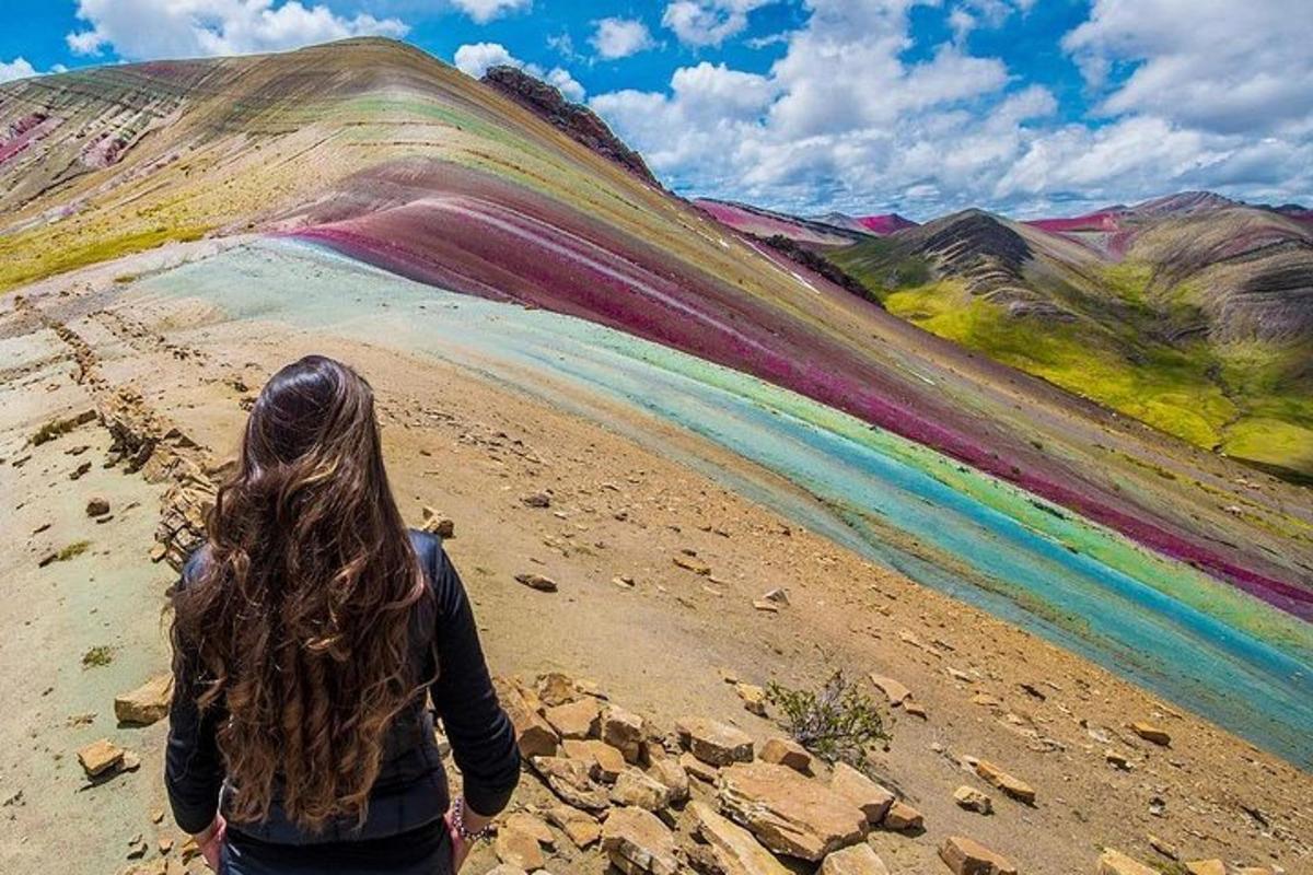 una donna in piedi su una strada sterrata che guarda una collina arcobaleno