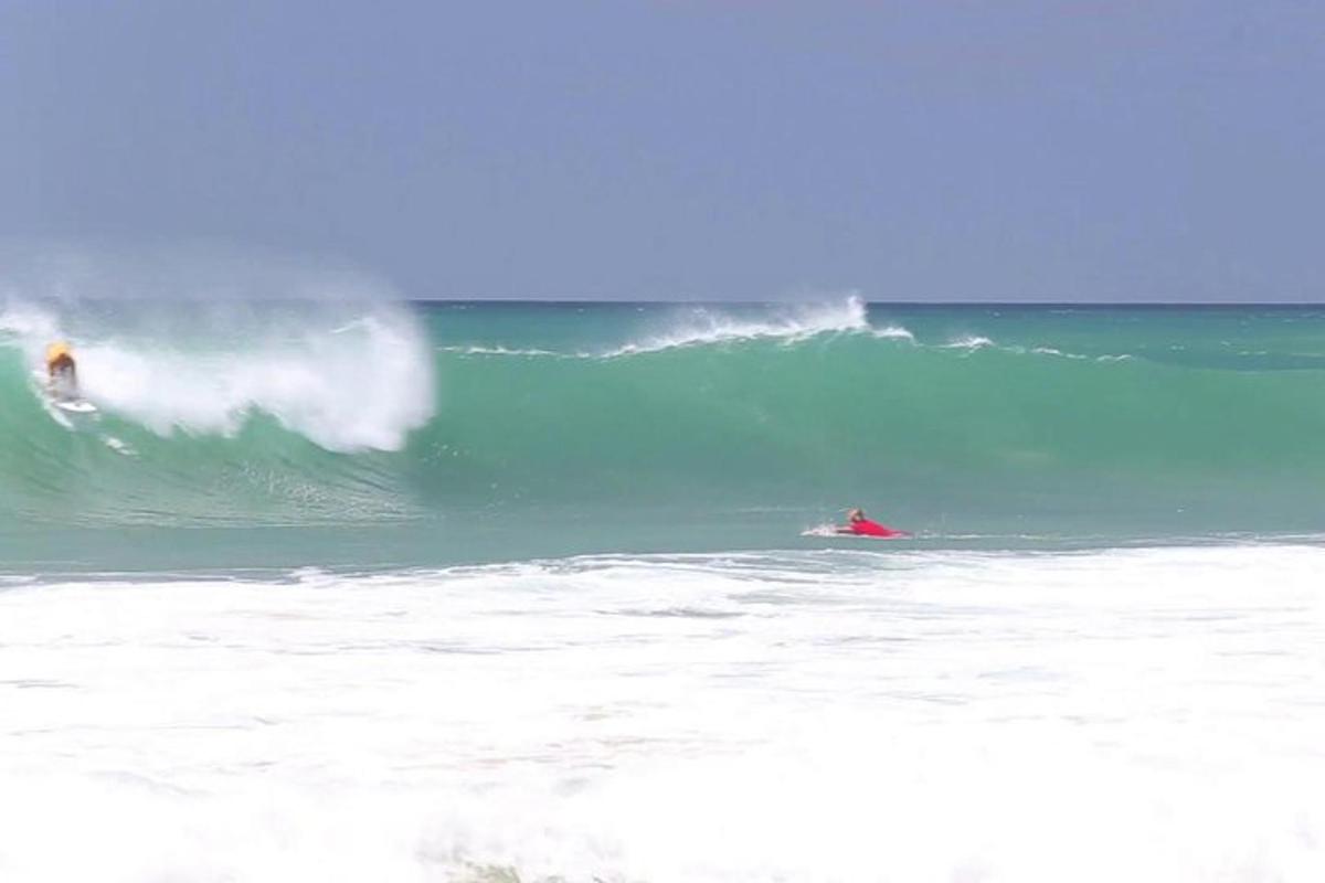 Două persoane pe plăci de surf călărind un val în ocean