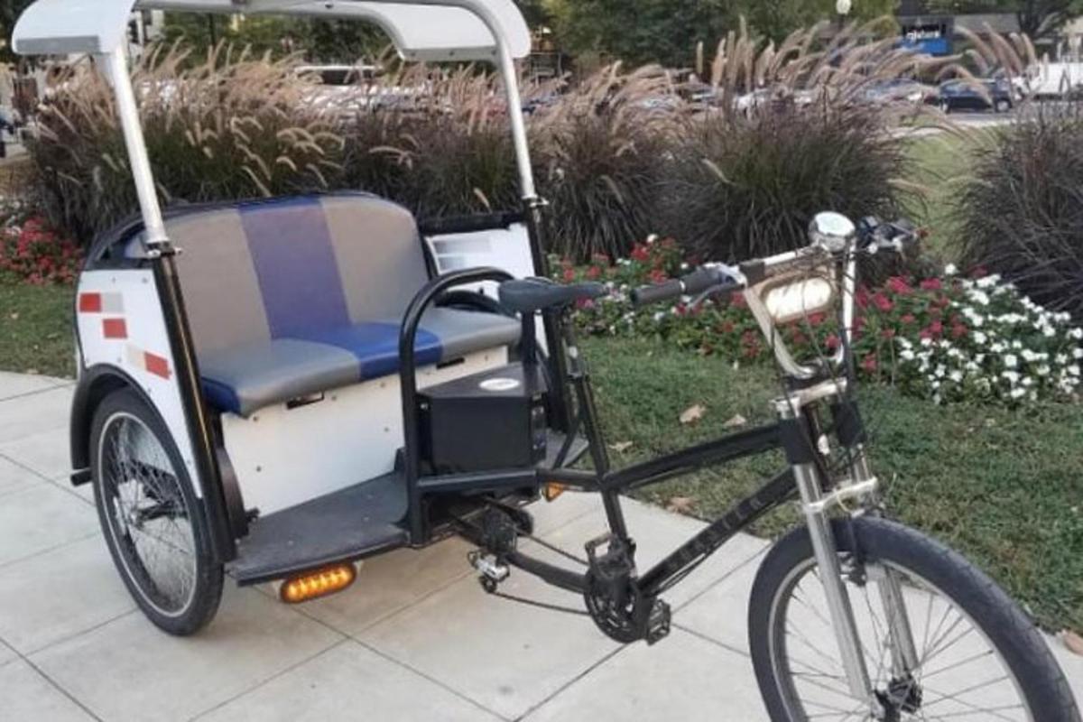 una bicicleta tirant d'un carret de golf per una vorera