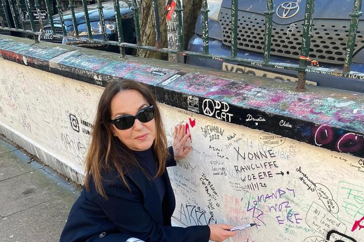 sieviete sēž blakus sienai ar grafiti
