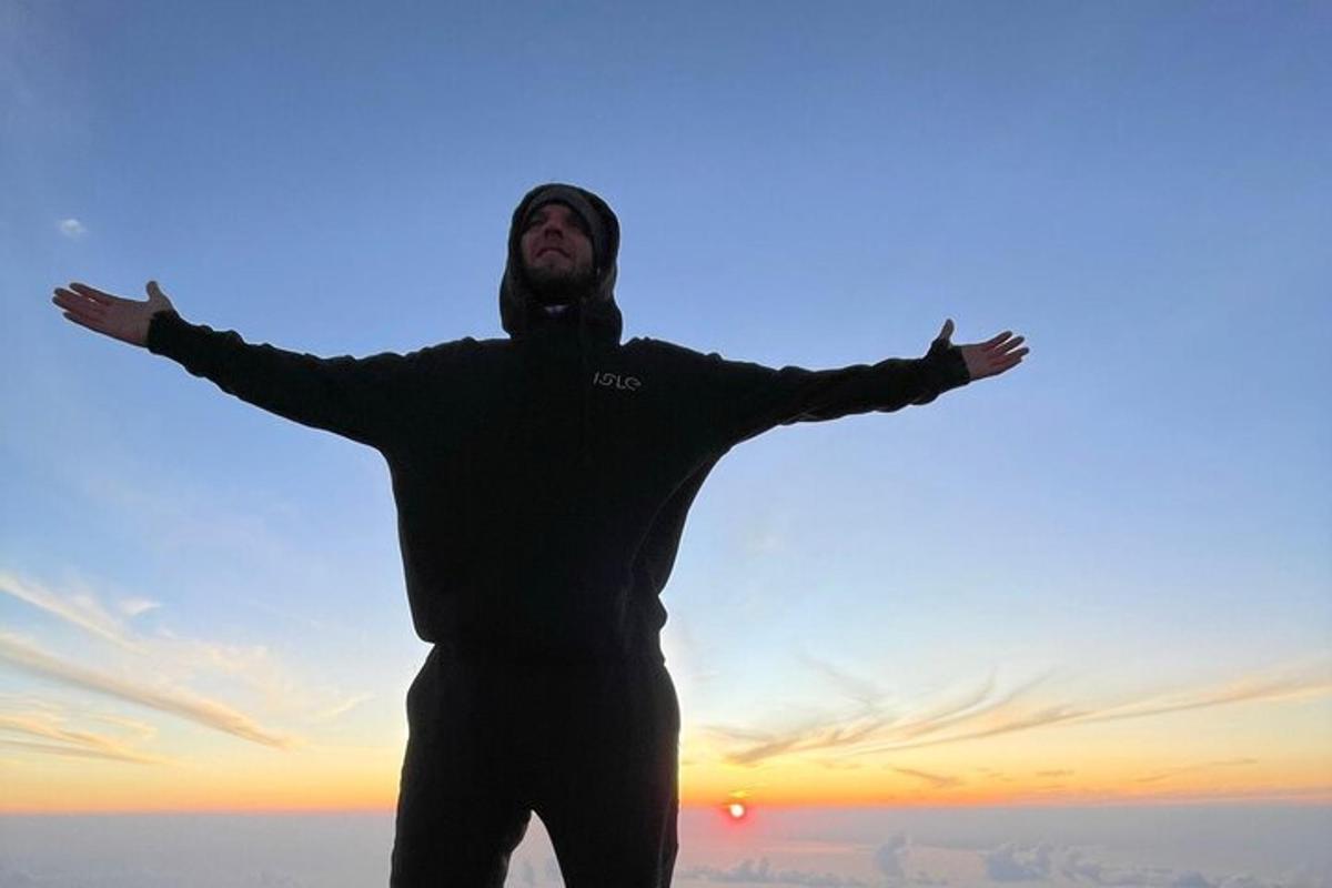 muž stojící s rozpaženýma rukama před západem slunce