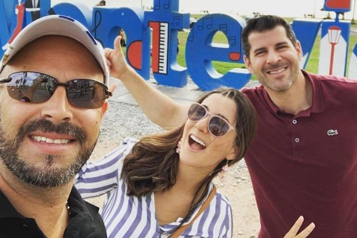 two men and a woman posing for a picture on the beach