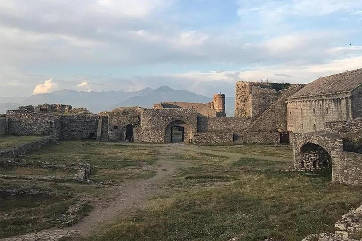 un edifici antic en un camp amb muntanyes al fons