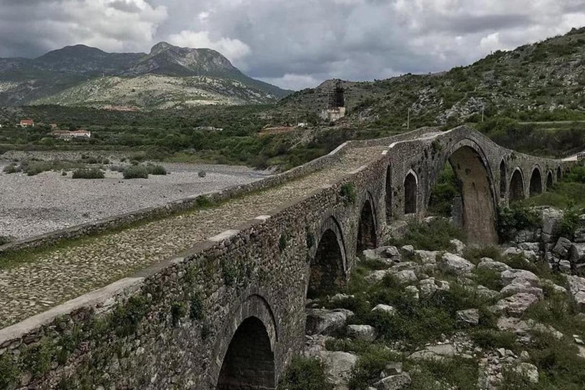 un pont de pedra sobre un riu amb muntanyes al fons