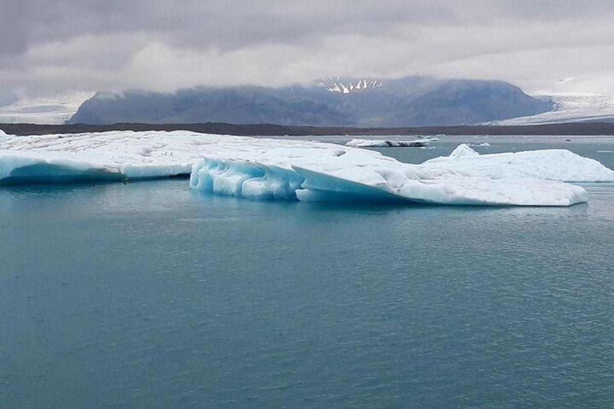 um grande iceberg flutuando na água com montanhas ao fundo