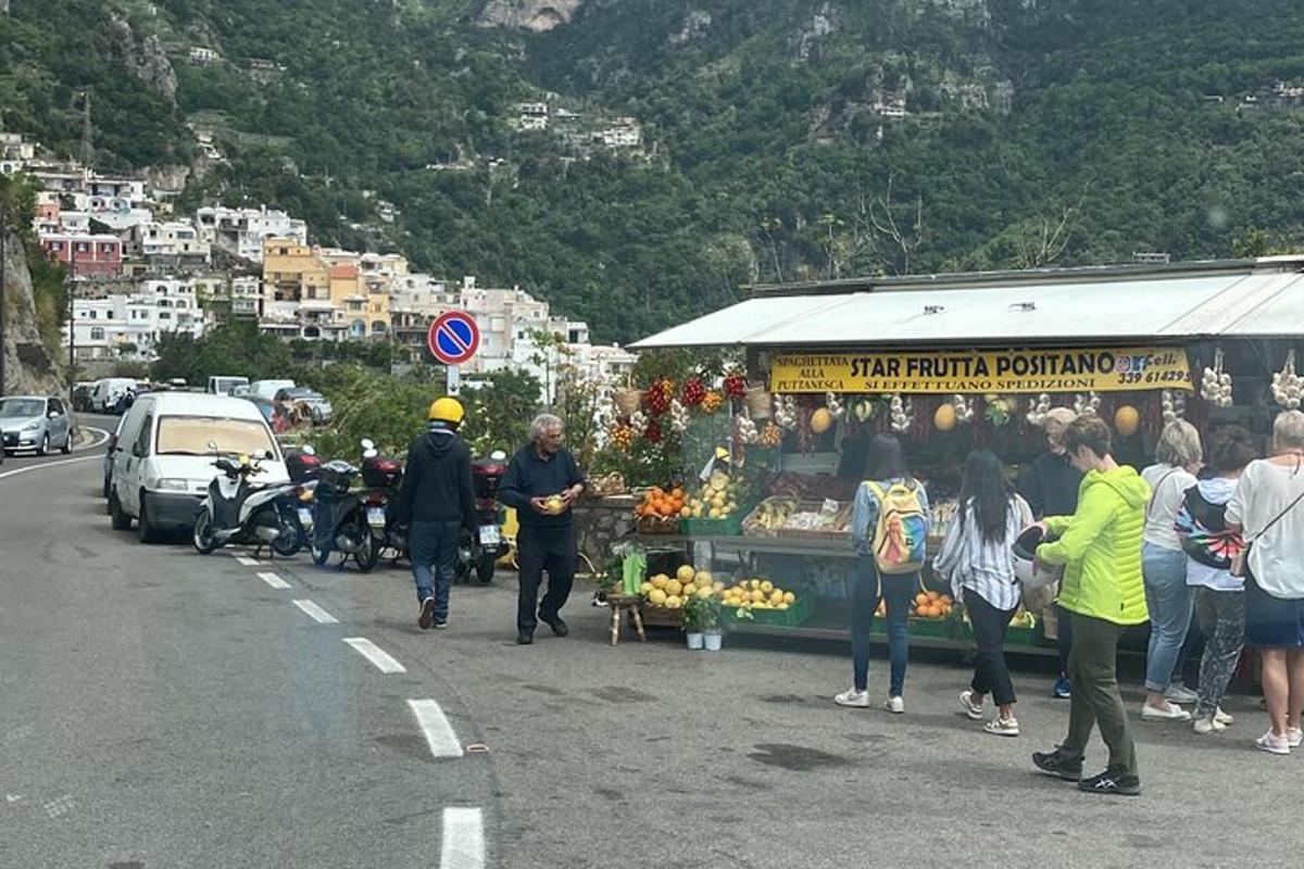μια ομάδα ανθρώπων που περπατούν γύρω από έναν πάγκο με φρούτα στην άκρη ενός δρόμου