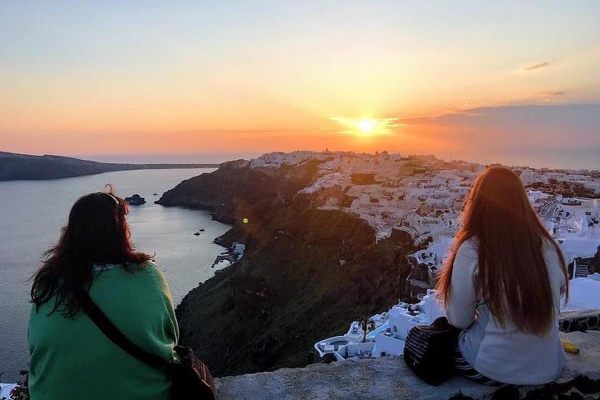 Dos mujeres sentadas en un acantilado mirando la puesta de sol
