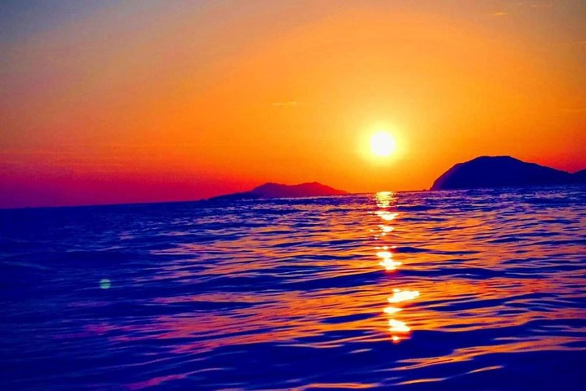 Západ slunce nad oceánem s horami v pozadí