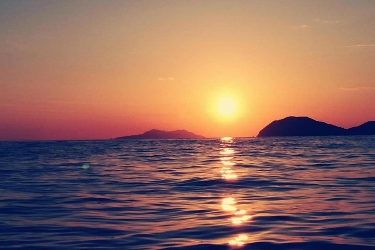 Západ slunce nad oceánem s horami v pozadí