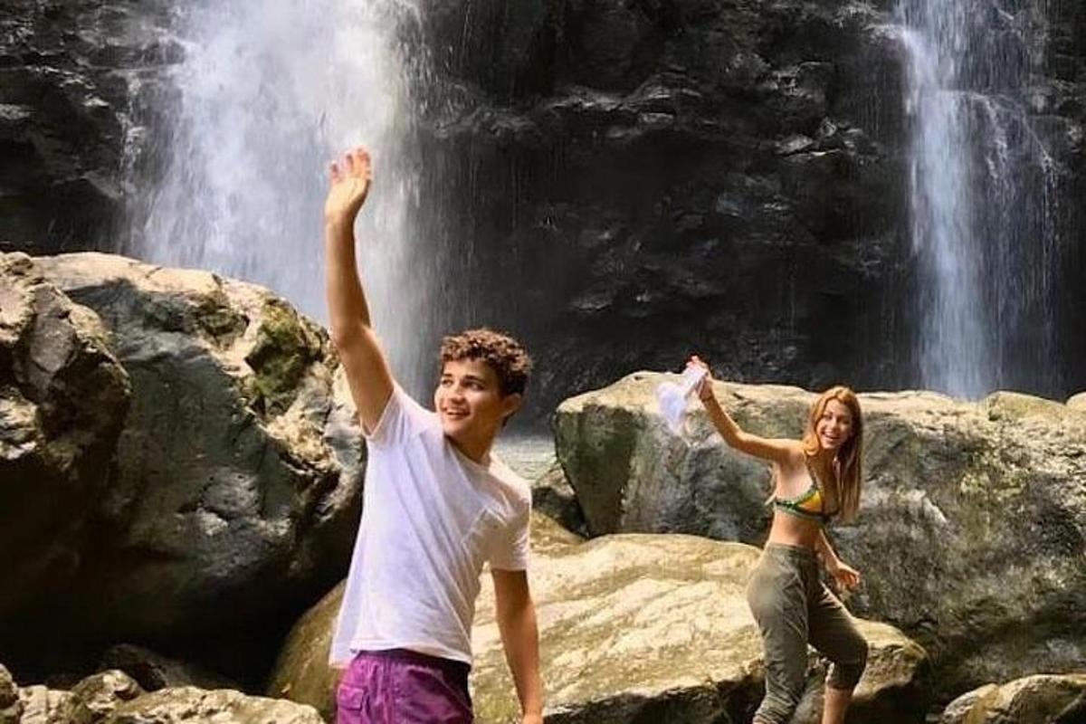 Dos personas de pie sobre rocas frente a una cascada.