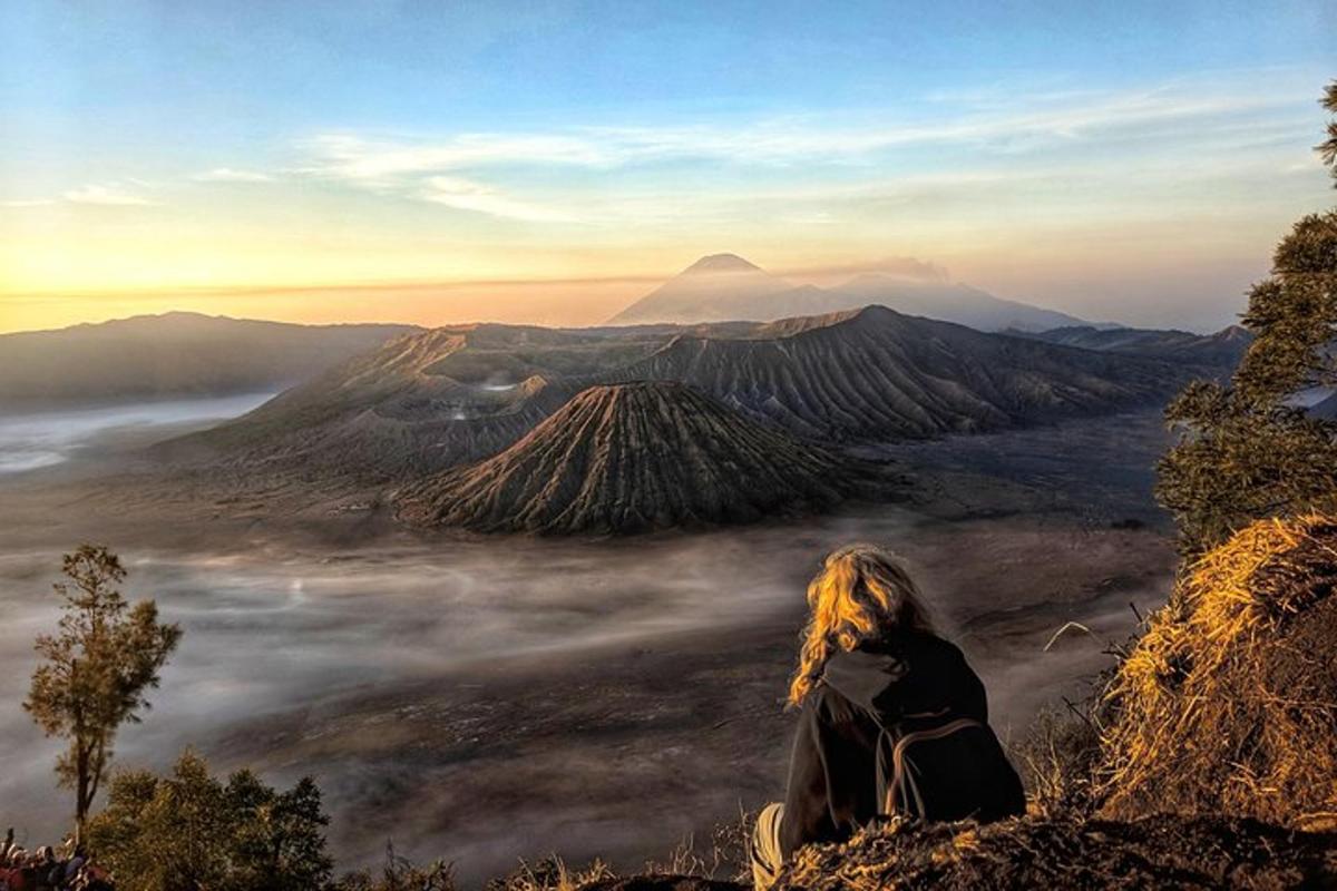 a woman sitting on top of a mountain looking at the clouds
