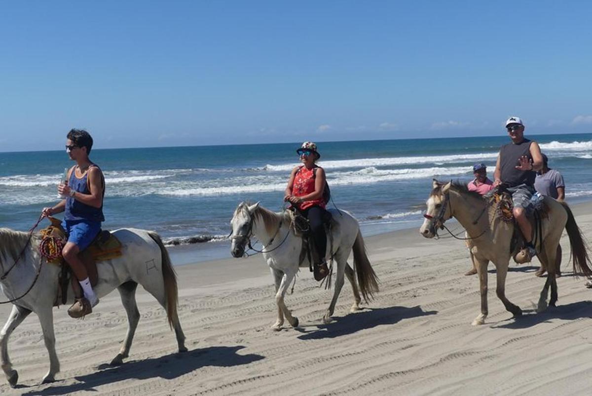 a group of people riding horses on the beach