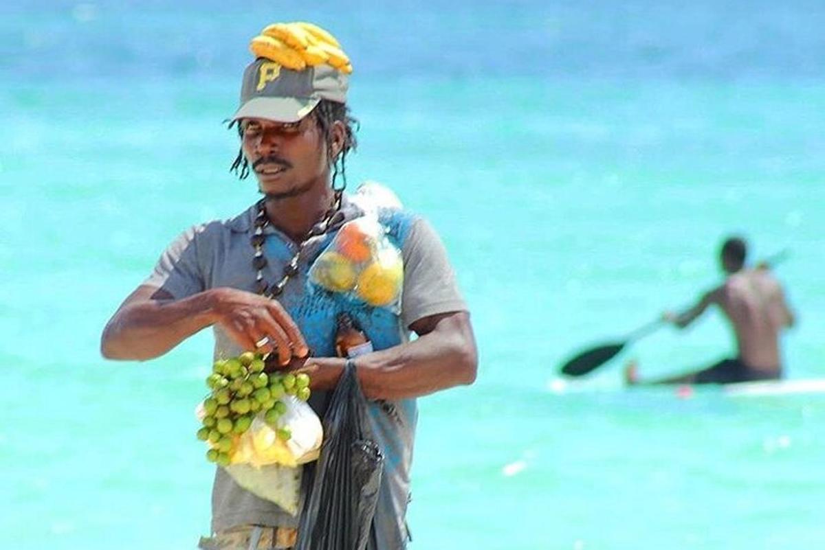 en mann som står på stranden og holder en haug med bananer