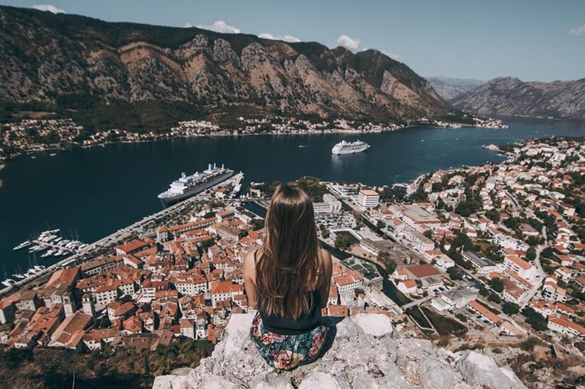 a woman sitting on top of a rock overlooking a city