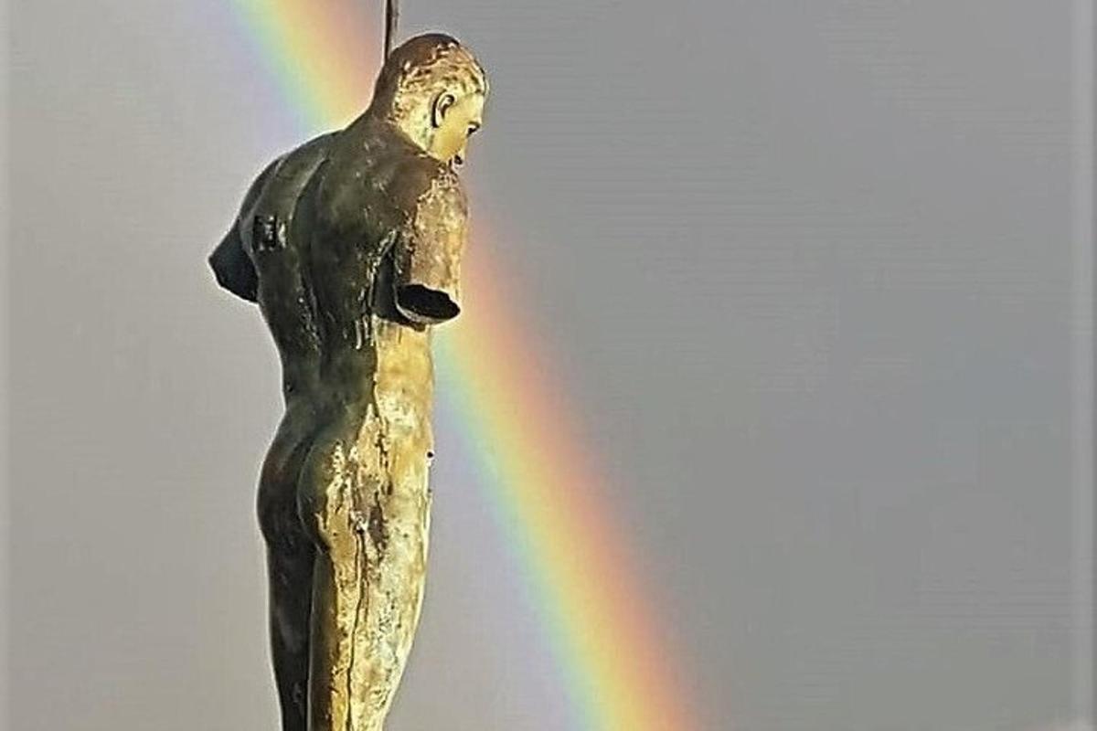 Una estatua de un hombre con un arcoíris al fondo.