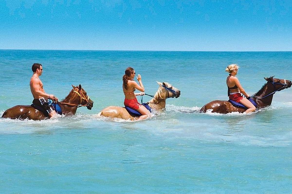 três pessoas andando a cavalo na água na praia