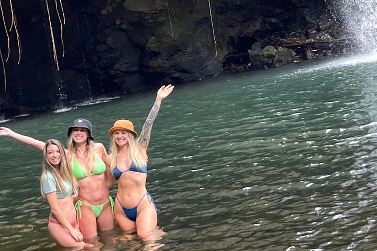 tiga wanita berdiri di dalam air berhampiran air terjun