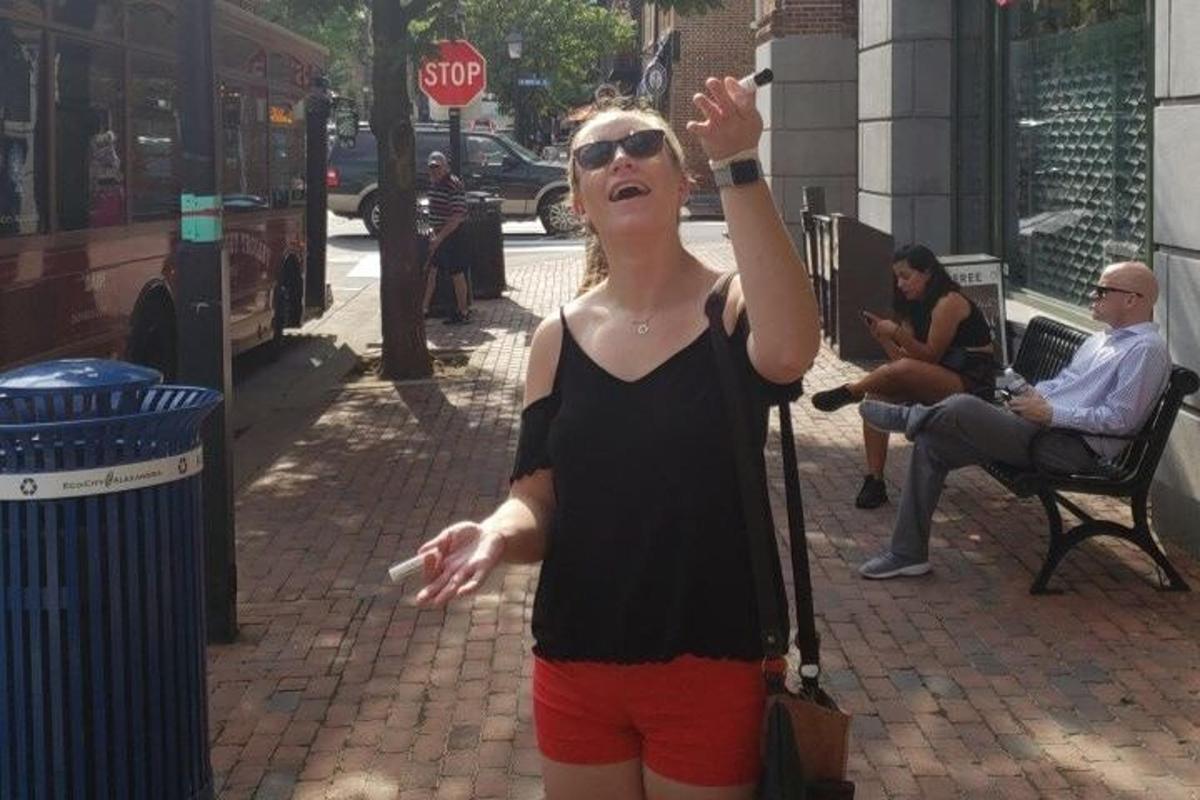 a woman standing on a sidewalk holding a wii remote