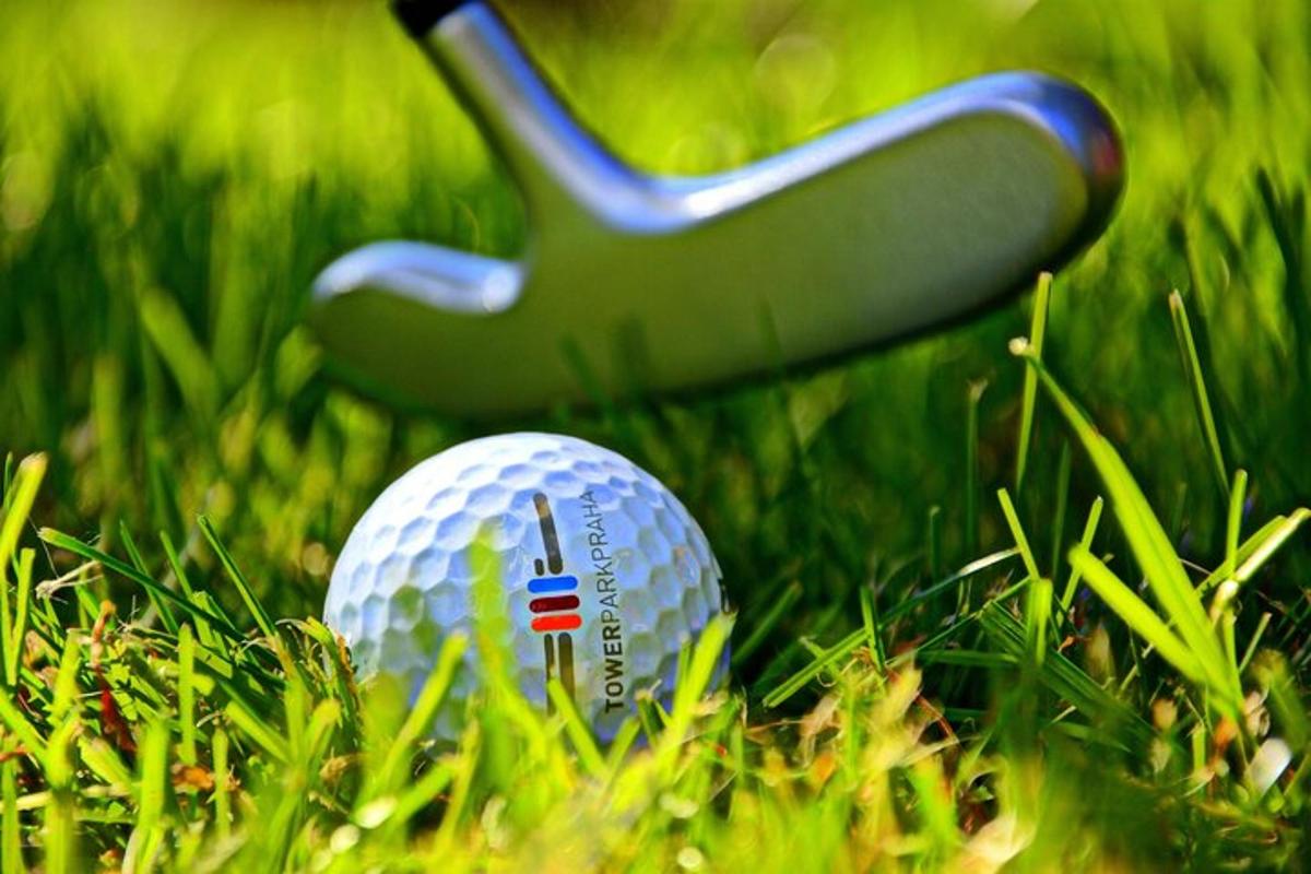 Una pelota de golf en el césped junto a un palo de golf.