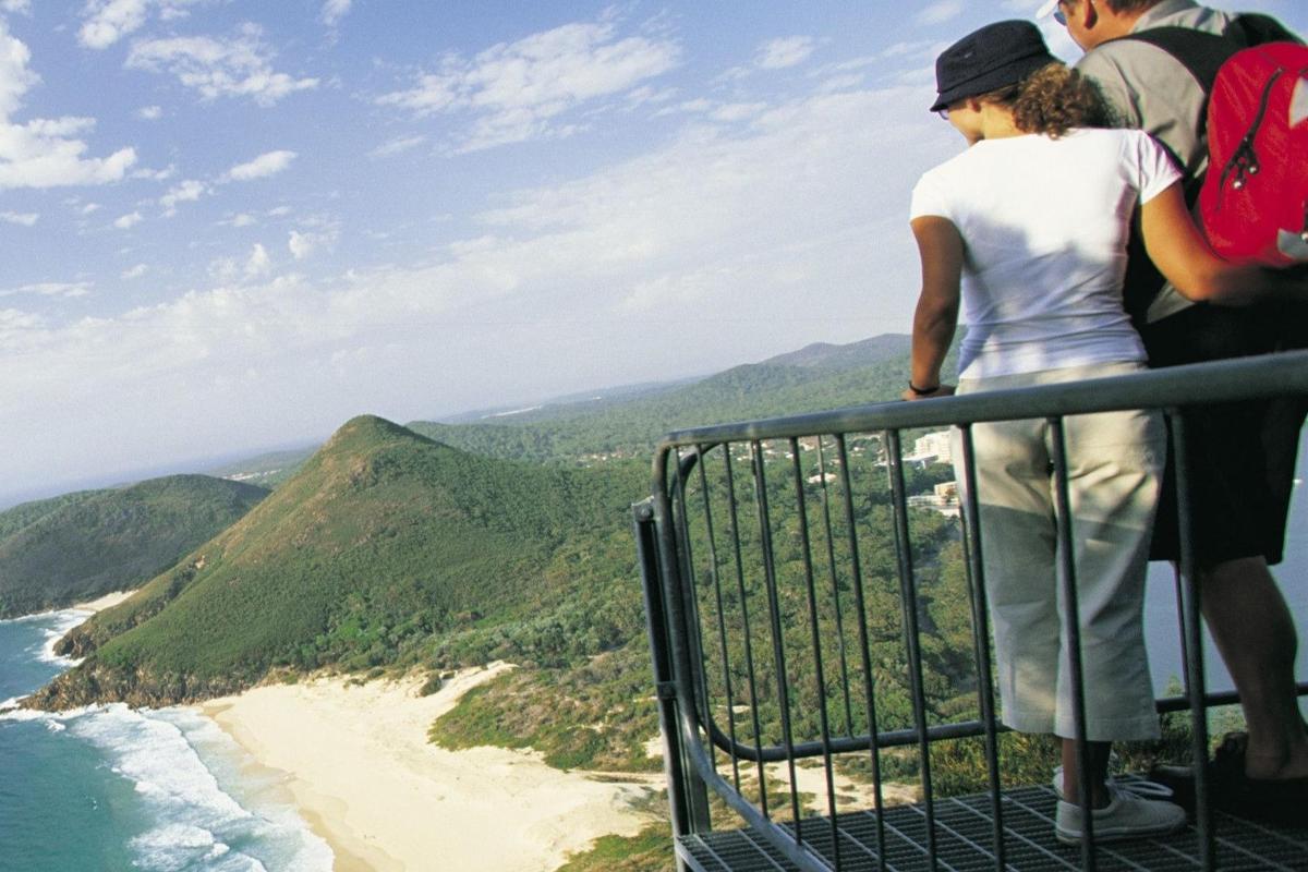 a group of people standing on the edge of a mountain overlooking a beach