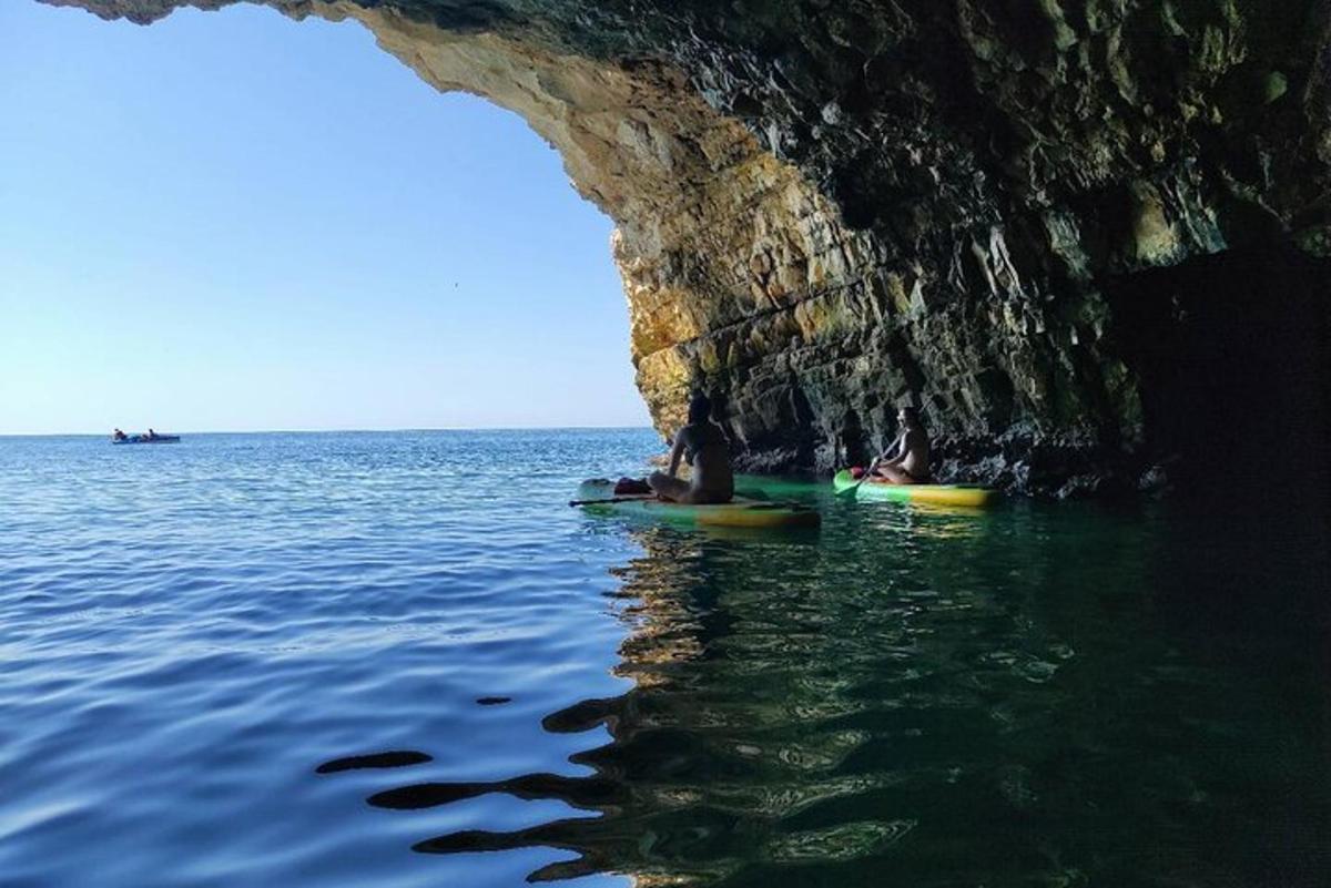 two people on kayaks in the water near a cave