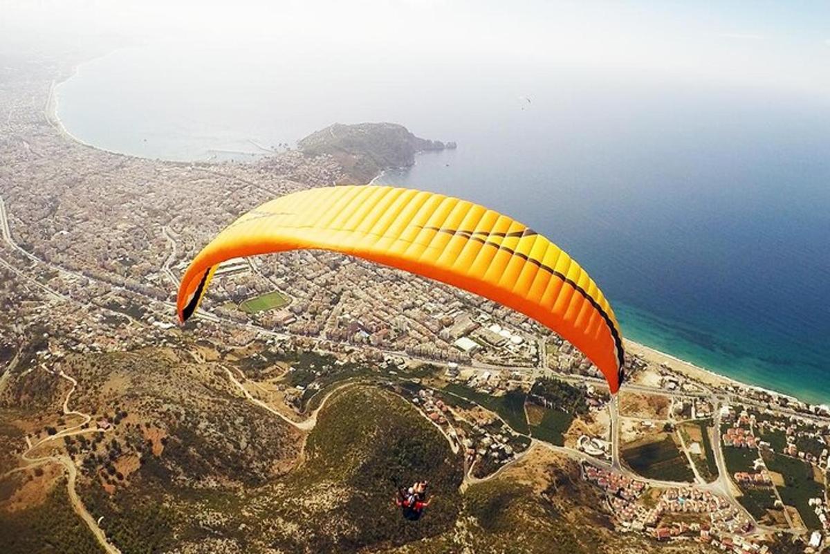 a person riding a yellow and orange parachute over the ocean