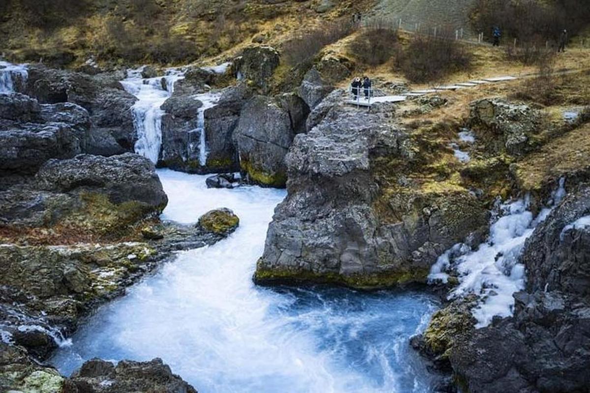 Dos personas paradas frente a una cascada en un río.