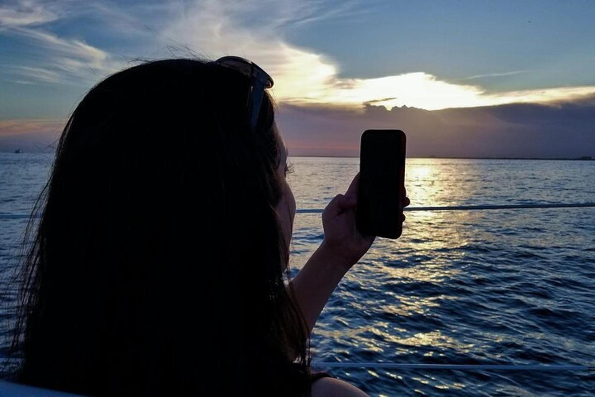 o femeie care fotografiază apusul de soare pe o barcă