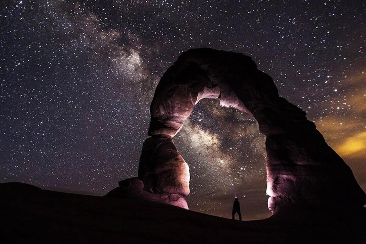 a person standing under a rock formation with the milky way