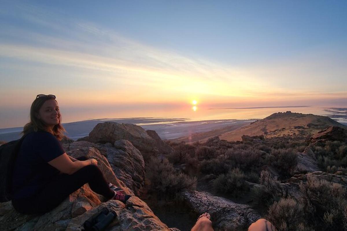 a woman sitting on top of a mountain watching the sunset