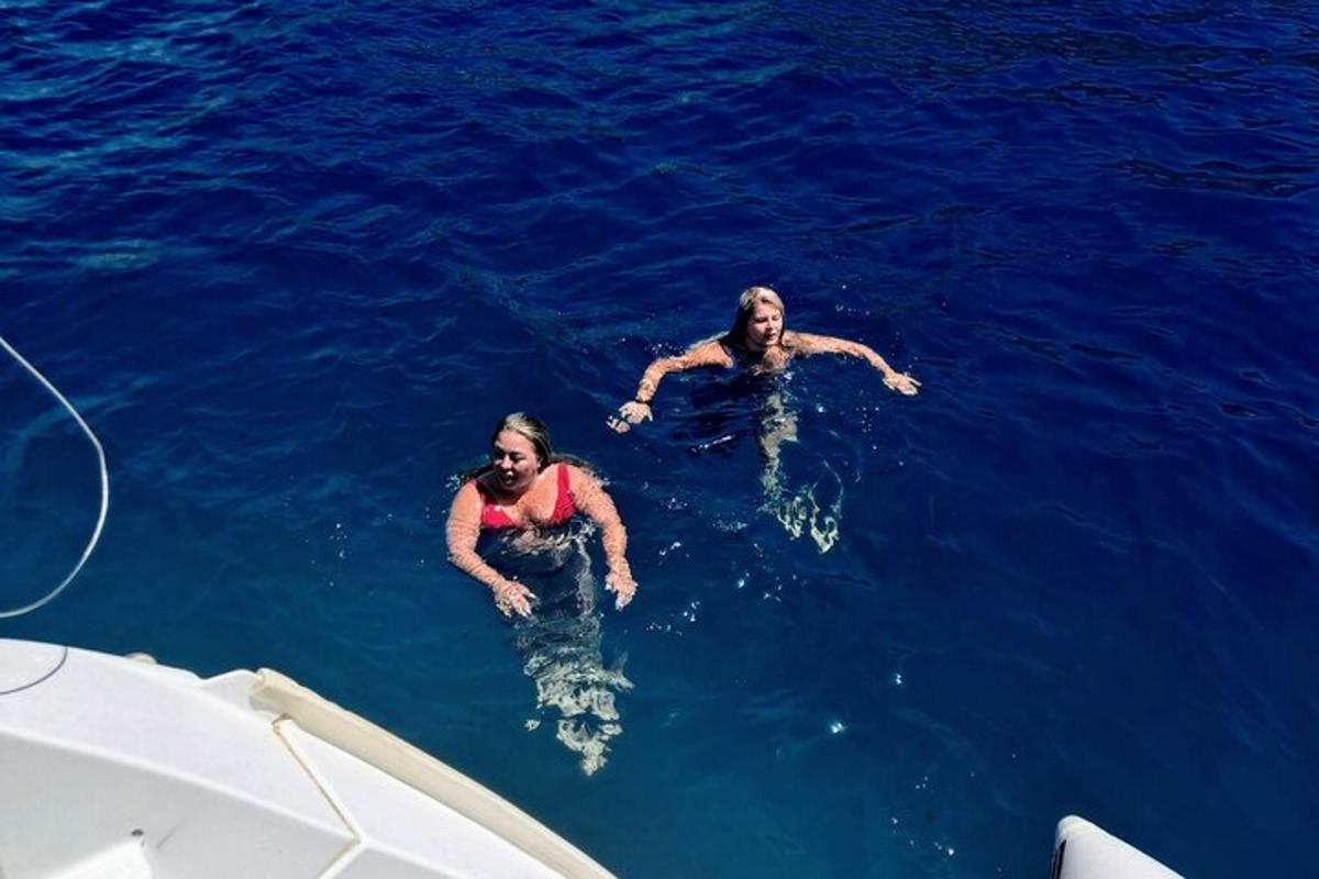 Dos personas nadando en el agua junto a un barco.