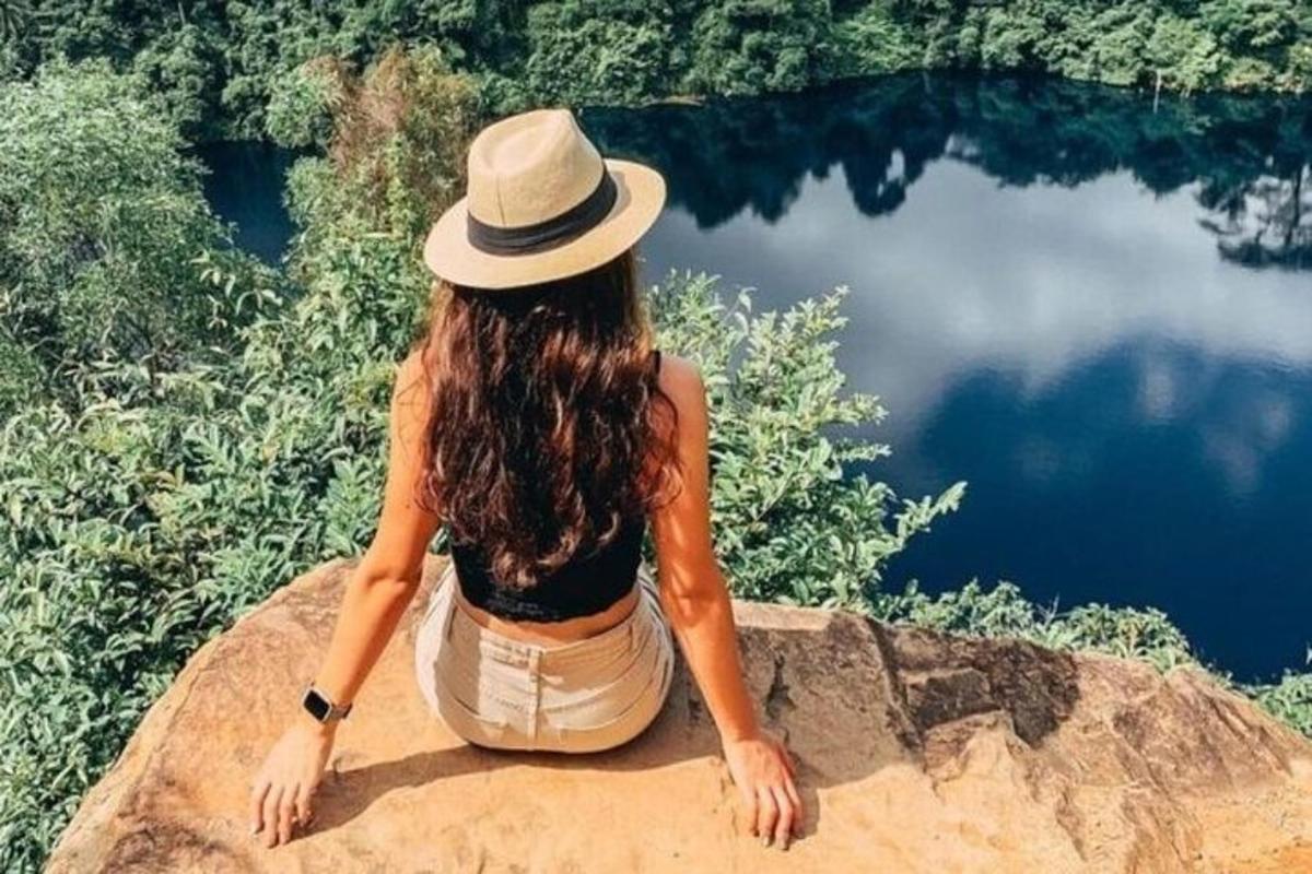 una dona amb barret asseguda en una roca al costat d'un llac