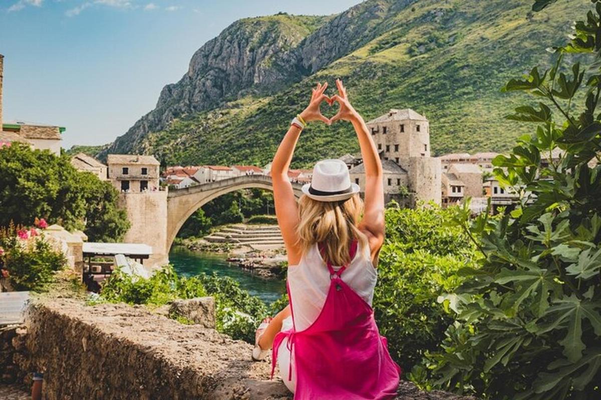 uma mulher de vestido rosa sentada em um muro olhando para uma ponte