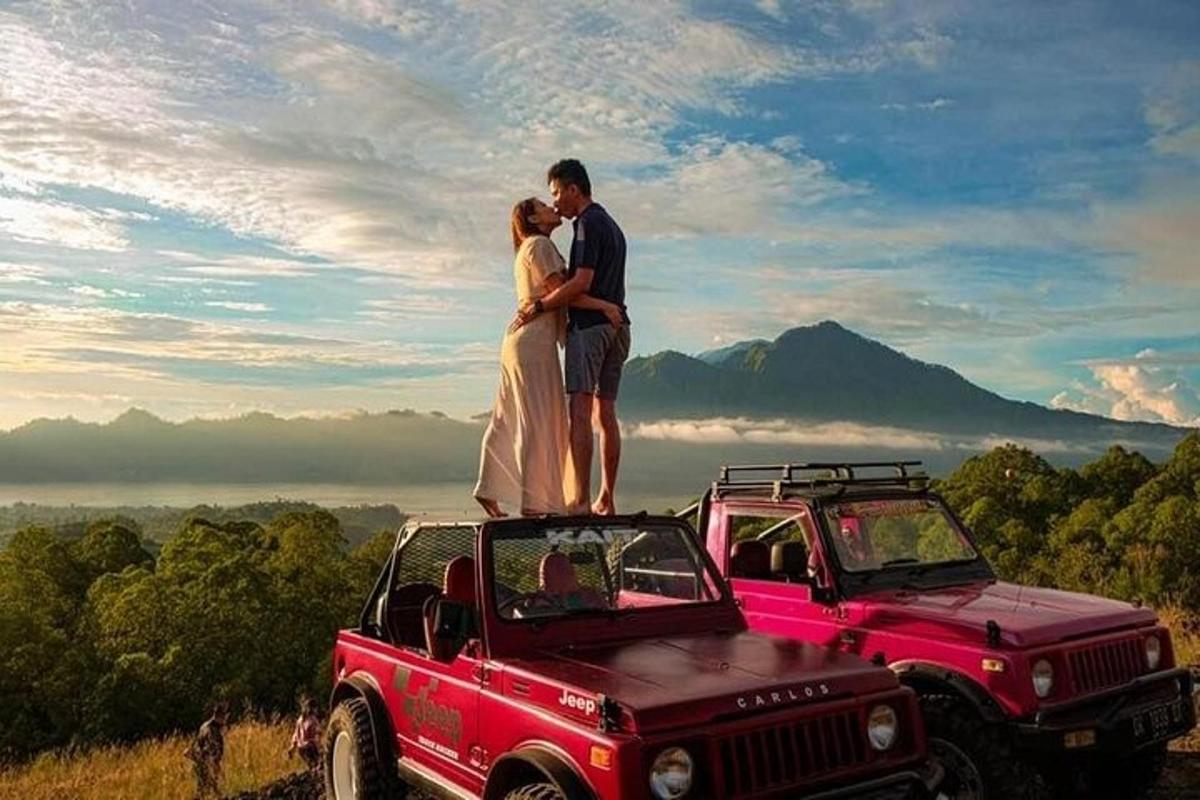 một cặp đôi đứng trên nóc xe jeep màu đỏ