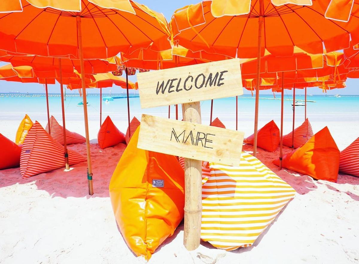 a welcome sign on a beach with orange umbrellas