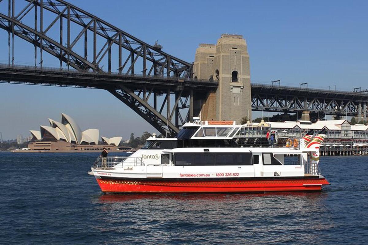 a red and white boat in the water near a bridge