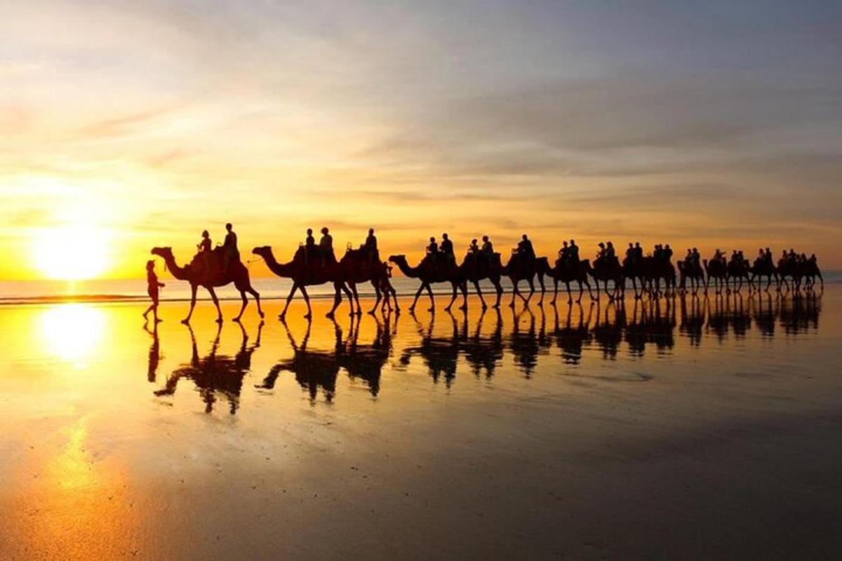 eine Gruppe von Menschen, die bei Sonnenuntergang auf Kamelen am Strand reiten