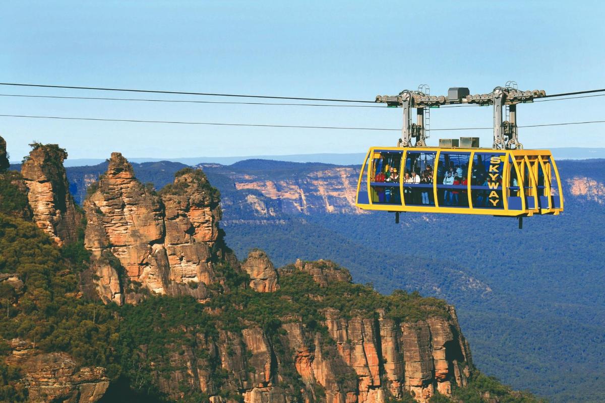 a yellow cable car flying over the blue mountains