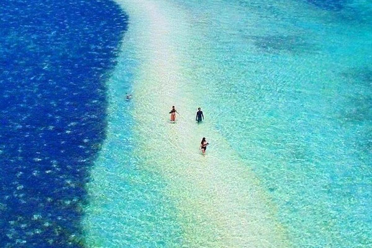 three people walking on a white beach in the ocean