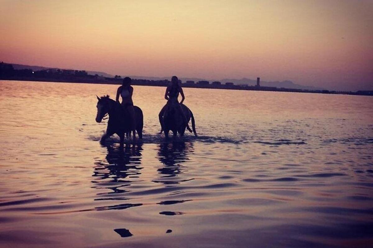 Dos personas están montando a caballo en el agua.