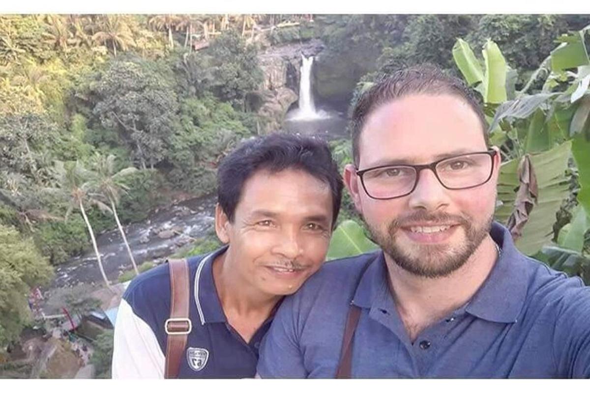 dua pria berpose untuk foto di depan air terjun