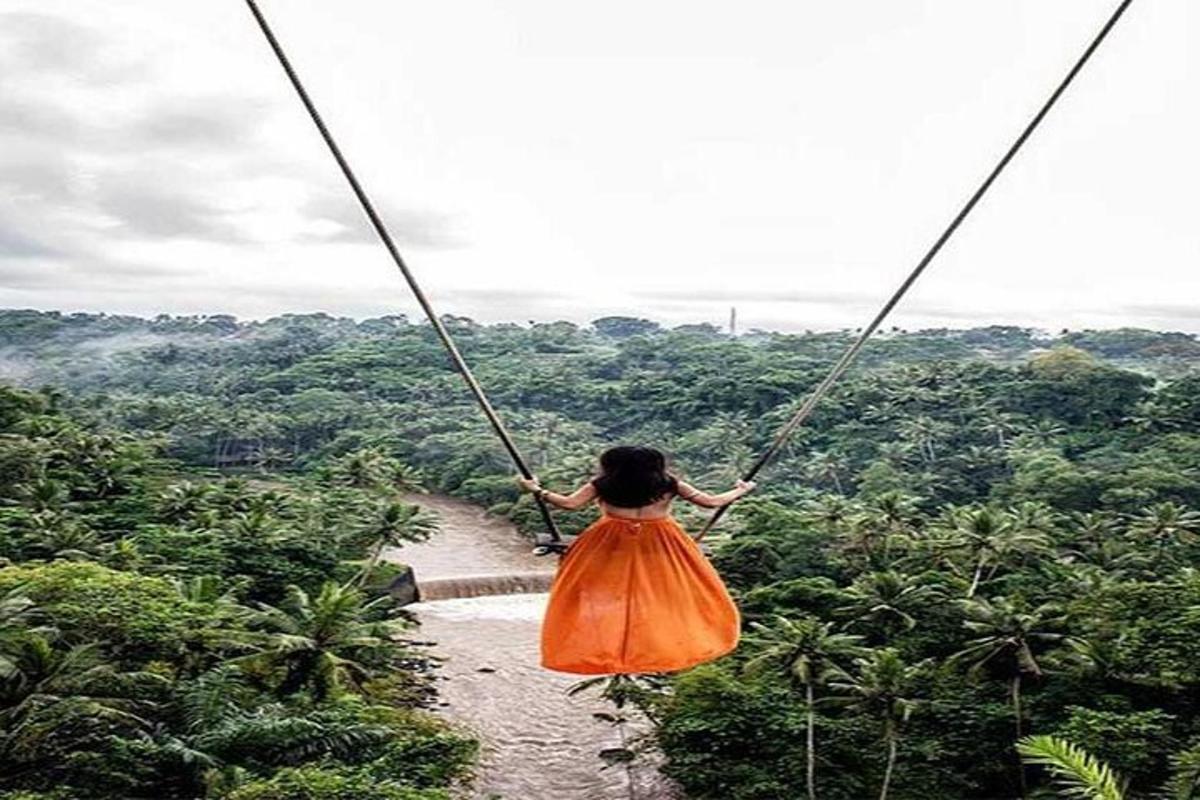 a woman in an orange dress swinging on a rope swing