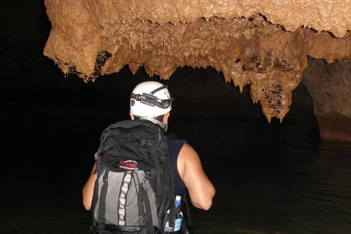 una persona a l'aigua amb una motxilla davant d'una cova