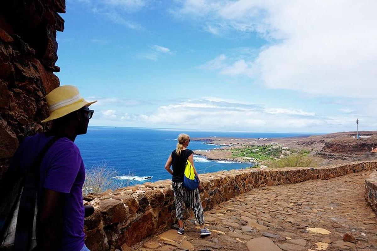 two people standing on a wall looking at the ocean