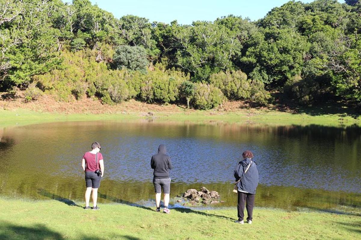 três pessoas em pé na grama perto de um lago