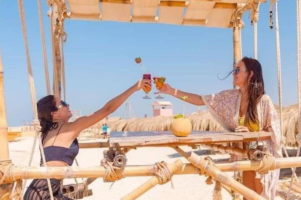 two women sitting at a table on the beach with drinks